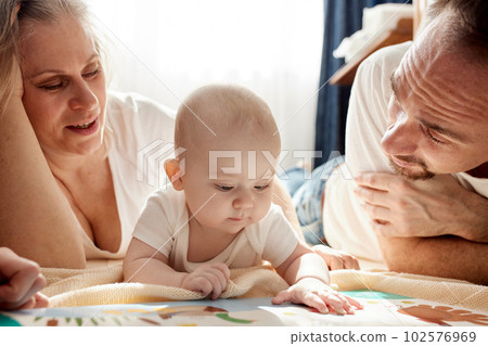 Close-up view of young parents, mom and dad, reading a children's book to their baby. Family training and education concept. Close-up. Close-up view of young parents, mom and dad, reading a children's book to their baby. Family training and education concept. Close-up. 102576969