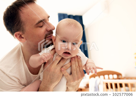 Close-up portrait of happy young father hugging and kissing his sweet adorable newborn child. Indoors shot, concept image. Copy space. 102577006