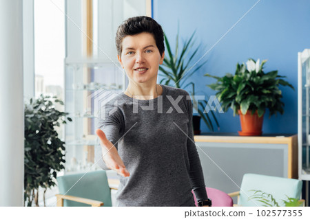 Polite friendly middle aged neutral gender hr manager recruiter posing for portrait looking at camera stretching hand to spectator proposing handshaking inviting for job interview welcoming in office. Polite friendly middle aged neutral gender hr manager recruiter posing for portrait looking at camera stretching hand to spectator proposing handshaking inviting for job interview welcoming in office. 102577355