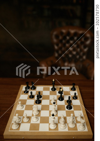 Chessboard with white and black pieces on wooden table with armchair 102578730