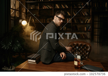 Serious pensive man sitting on table with alcohol glass looking at camera Serious pensive man sitting on table with alcohol glass looking at camera 102578736