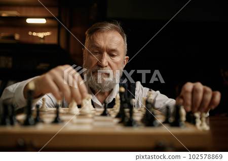 Face portrait of senior man moving chess piece on board during competition match 102578869