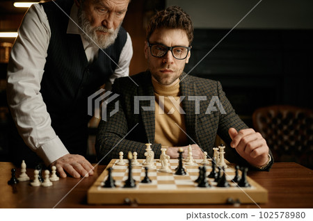Senior man teaching young guy playing chess explaining rules of game Senior man teaching young guy playing chess explaining rules of game 102578980
