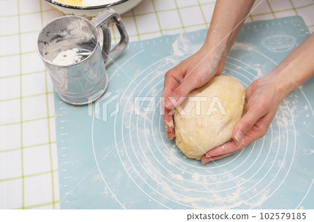 A woman kneads the dough with her hands, the hands of a baker, a silicone mat, a sieve, handmade baking. View from above. 102579185