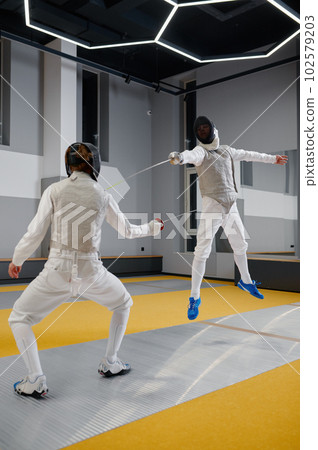 Two fencers sparring during training session in professional martial art school Two fencers sparring during training session in professional martial art school 102579203