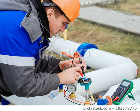 A Caucasian electrician in a helmet measures the voltage on the sensors of a gas distribution 102579770