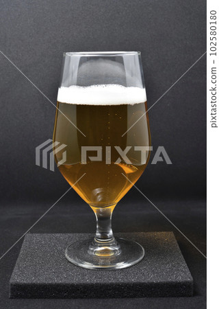 A glass of light beer on a black background. Fresh beer from a glass. A glass of light beer on a black background. Fresh beer from a glass. 102580180