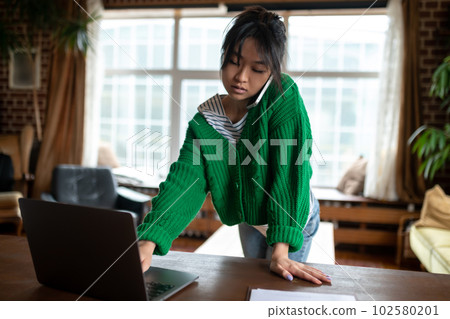 Girl in green shirt talking on the phone and switching on laptop Girl in green shirt talking on the phone and switching on laptop 102580201