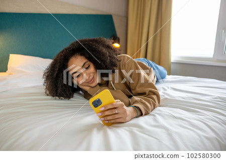 Dark-haired young woman with a phone in hands on the bed 102580300