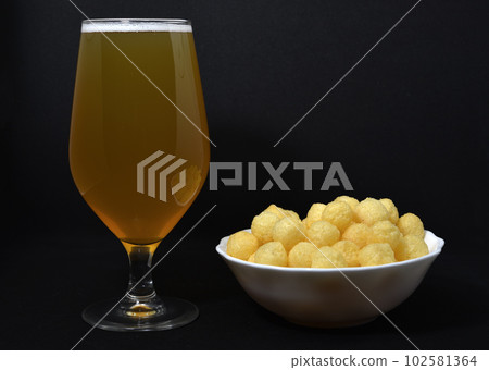 A glass of light beer and a snack on a plate. Beer with a snack. Salted corn snack. 102581364
