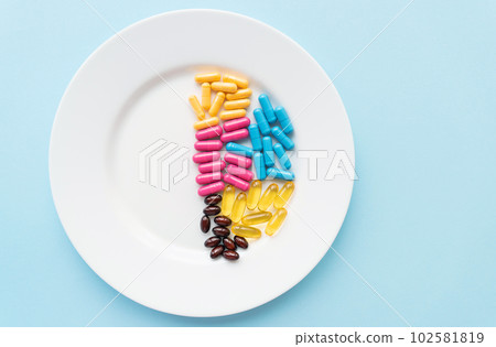 Food supplements-capsules of bright color lie on a white plate in a heap. Concept of medicine and health. 102581819
