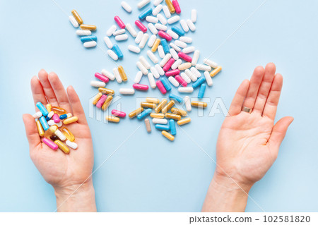 The girl holds a handful of bright vitamins, nutritional supplements and medicines in her palms on a blue background. Concept of medicine and healthcare. 102581820