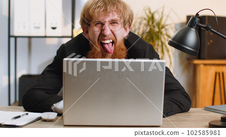 Office businessman hiding behind laptop computer making funny silly face fooling around, disrespect Office businessman hiding behind laptop computer making funny silly face fooling around, disrespect 102585981