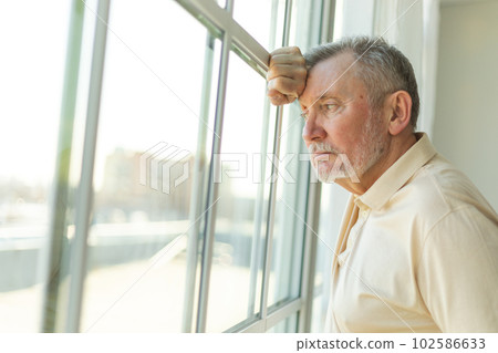 Sad tired lonely disappointed older senior man at home alone. Unhappy grandfather looking sadly outside window experiencing grief relative death bad news. Stressed elder man suffering from loneliness 102586633