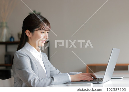 A woman in a gray suit who smiles at her desk_1 A woman in a gray suit who smiles at her desk_1 102587203
