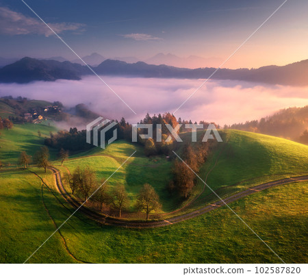 Aerial view of alpine meadows and mountains in clouds at sunrise Aerial view of alpine meadows and mountains in clouds at sunrise 102587820