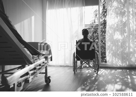 The woman sitting on wheelchair. She is see window with patient bed in hospital.disabled person lonely. Photo concept depression and Patient. The woman sitting on wheelchair. She is see window with patient bed in hospital.disabled person lonely. Photo concept depression and Patient. 102588611