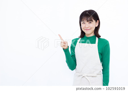 A housewife in her thirties in an apron who raises her index finger in front of a white background 102591019