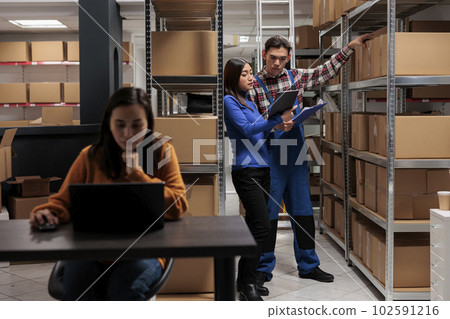 Warehouse worker and logistics manager doing products audit in storage room. Storehouse employees managing goods parcels quality control while analyzing data in clipboard and digital tablet 102591216