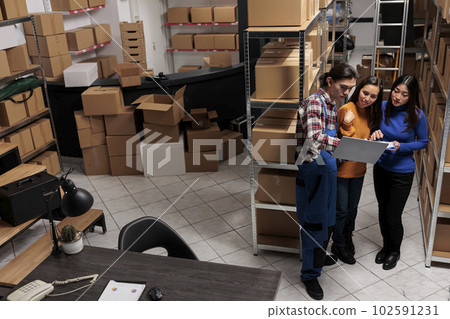 Delivery asian managers team optimizing warehouse operations on laptop together. Storehouse man and women employees coworking, managing logistics and distribution in storage room top view 102591231