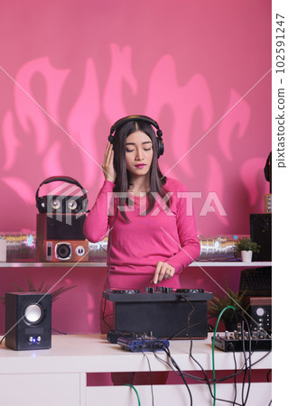 Asian musician standing at dj table creating musical performance with remix music using professional mixer console. Artist performer performing techno song, enjoying nightlife in club Asian musician standing at dj table creating musical performance with remix music using professional mixer console. Artist performer performing techno song, enjoying nightlife in club 102591247