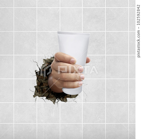 Human hand holding a cosmetics bottle through the wall with cracks Human hand holding a cosmetics bottle through the wall with cracks 102592842