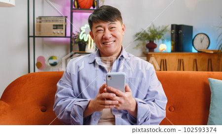 Asian chinese adult man sitting on sofa, using smartphone share messages on social media application 102593374