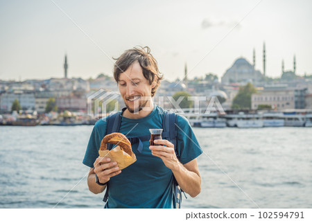 Man in Istanbul having breakfast with Simit and a glass of Turkish tea. Glass of Turkish tea and bagel Simit against golden horn bay in Istanbul, Turkey. Turkiye Man in Istanbul having breakfast with Simit and a glass of Turkish tea. Glass of Turkish tea and bagel Simit against golden horn bay in Istanbul, Turkey. Turkiye 102594791