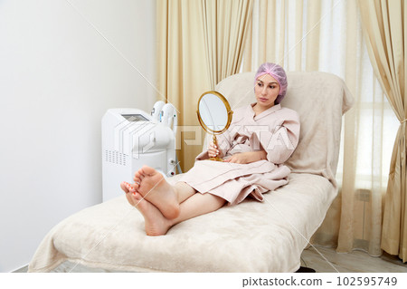 Young woman sitting in medical chair and looking in the mirror. She is satisfied after successful beauty treatment Young woman sitting in medical chair and looking in the mirror. She is satisfied after successful beauty treatment 102595749
