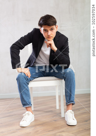 Charismatic young man sitting on chair in the middle of the room Charismatic young man sitting on chair in the middle of the room 102597034