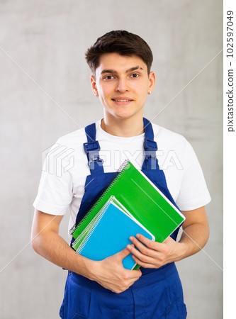 Positive worker in blue jumpsuit poses with large stack of notebooks. 102597049
