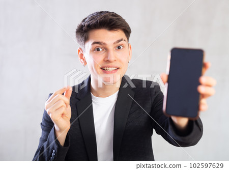Agent in black suit jacket shows dark empty mobile phone screen and points at device with his hand 102597629