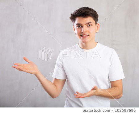 Surprised young man with pointing hand gestures standing against background of light unicolored wall 102597696