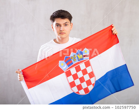 Calm young man holding flag of Croatia against unicoloured background Calm young man holding flag of Croatia against unicoloured background 102597750