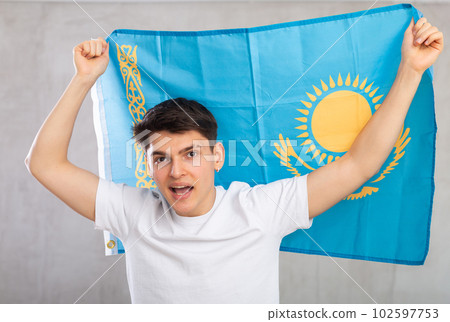 Happy young man holding flag of Kazakhstan against unicoloured background Happy young man holding flag of Kazakhstan against unicoloured background 102597753
