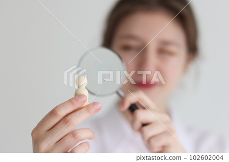 Woman looks at wooden figurine in hand through loupe Woman looks at wooden figurine in hand through loupe 102602004
