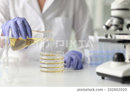 Assistant pours yellow liquid from flask at desk in lab Assistant pours yellow liquid from flask at desk in lab 102602020