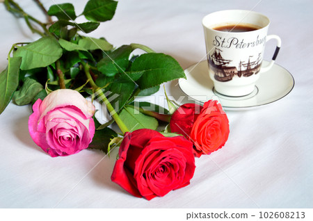 Cup of coffee and red roses on a white tablecloth. Cup of coffee and red roses on a white tablecloth. 102608213