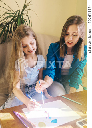 Mother and daughter paint. Art teacher teaches the technique of applying watercolor paint, gouache and teaches how to hold the brush correctly. Happy childhood concept. Smiling people. Fun mood. Mother and daughter paint. Art teacher teaches the technique of applying watercolor paint, gouache and teaches how to hold the brush correctly. Happy childhood concept. Smiling people. Fun mood. 102611184