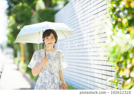 A middle-aged woman walking with a parasol in the summer sun A middle-aged woman walking with a parasol in the summer sun 102612328