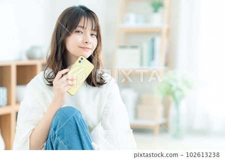 坐在客廳裡操作智能手機的年輕女性 102613238