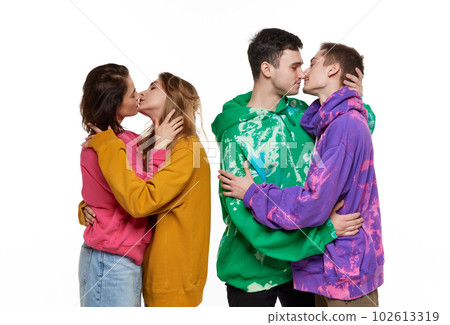 Portrait of four young people, same sex couples in colorful hoodies posing, kissing over white background. LGBTQIA supporters Portrait of four young people, same sex couples in colorful hoodies posing, kissing over white background. LGBTQIA supporters 102613319