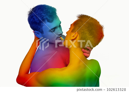 Portrait of two young men, couple hugging, eating jelly candy against white background. Models posing shirtless with rainbow colored body 102613328