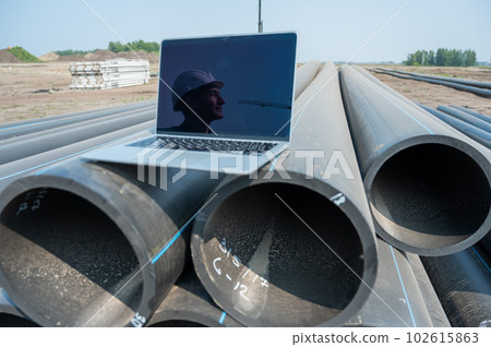 Laptop on pipes at a construction site. Reflection of a portrait of a builder in a helmet on the screen.  102615863