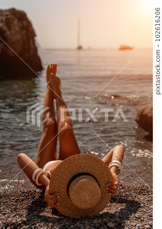 woman sea travel Tanned middle-aged woman with long hair and a white bathing suit. He sits on the seashore in a large sun hat with his back and looks at the sea. 102616206