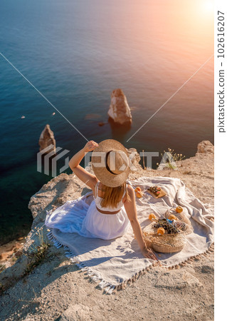 woman sea trevel. photo of a beautiful woman with long blond hair in a pink shirt and denim shorts and a hat having a picnic on a hill overlooking the sea woman sea trevel. photo of a beautiful woman with long blond hair in a pink shirt and denim shorts and a hat having a picnic on a hill overlooking the sea 102616207