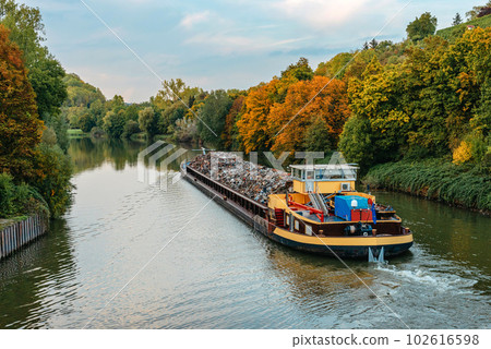 Transportation industry. Ship barge transports scrap metal and sand with gravel. Barge loaded with scrap metal is on the roadstead. Scrap metal transportation by water. Barge laden by metal salvage 102616598
