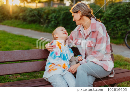 mother and son sit on a park bench in the rays of the setting sun. the concept of a family. Mother's Day. beautiful girl (mother) with a boy (son) in the park in the park are sitting on a bench at 102616603
