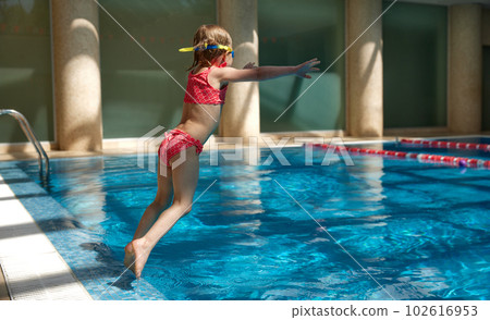Little baby, child, girl in swimming suit jumping into water, swimming into pool indoors on warm sunny day. 102616953