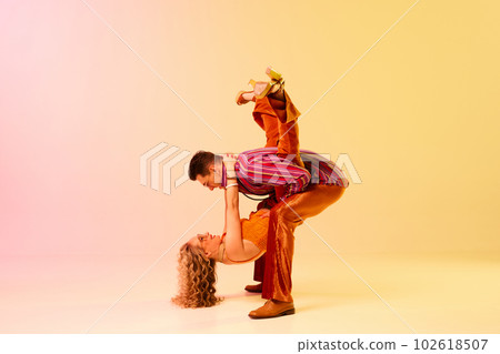 Dynamic image of stylish, talented, emotional couple, man and woman in vintage costumes dancing disco dance against gradient pink yellow background Dynamic image of stylish, talented, emotional couple, man and woman in vintage costumes dancing disco dance against gradient pink yellow background 102618507
